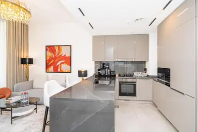 a kitchen with white cabinets and a living room at Escape24 Brand New 1BR with City View near Burj Khalifa in Dubai
