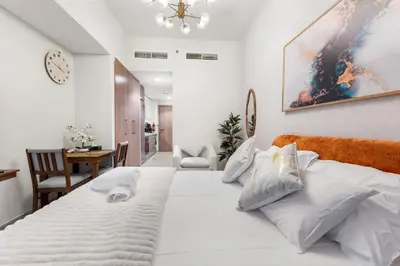 a bedroom with a large white bed with a clock on the wall at Cozy Luxe Studios in Meydan in Dubai