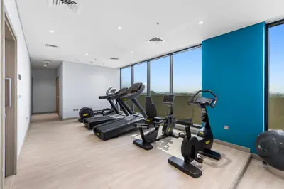 a gym with treadmills and ellipticals in a room with windows at Cozy Luxe Studios in Meydan in Dubai