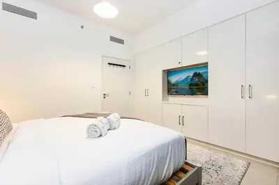 a white bedroom with a bed and a flat screen tv at FIRST CLASS 1BR Modern Comfort in the City in Dubai