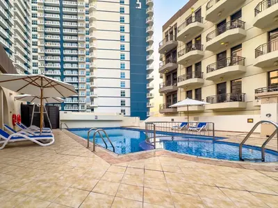 a swimming pool with chairs and an umbrella and some buildings at Dubai 1BR Balcony Views Near Miracle Garden in Dubai
