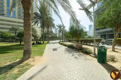 a sidewalk with a palm tree and a trash can at Vogue JVC Jeewar Tower near Circle Mall, One Bedroom Apartment with Balcony and City View, Access to all Amenities in Dubai