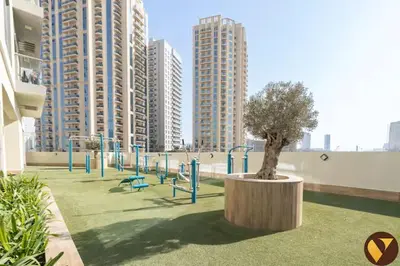 a playground with a tree in a park with buildings at Vogue JVC Jeewar Tower near Circle Mall, One Bedroom Apartment with Balcony and City View, Access to all Amenities in Dubai