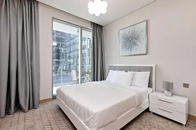 a white bedroom with a bed and a large window at Vida Dubai Mall Connected 2BR in Sabkhah