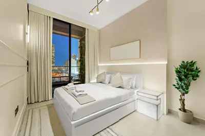 a white bedroom with a bed and a window at Bright & Cozy 1BR Apartment with Balcony in JVC in Dubai