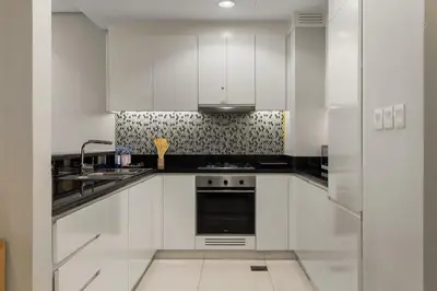 a kitchen with white cabinets and a black appliance at Gogoto4 - 2BR High Floor Burj View Infinity Pool PS5 NYE Fireworks View in Dubai
