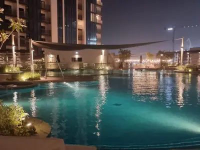 a large swimming pool at night with buildings at FAM Living -Bright & Spacious Home in Sobha Hartland in Dubai