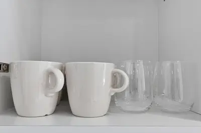 four white cups and glass vases sitting on a shelf at Golden Stays - Binghatti Crescent I Cozy 1BR Retreat I Pool & Gym I JVC Dubai in Dubai