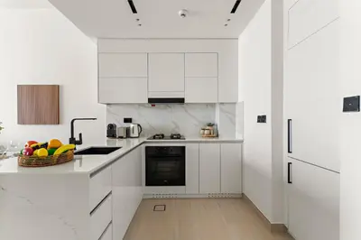 a white kitchen with white cabinets and a basket of fruit at VayK - Brand New and Bright 1BR in JVC in Dubai