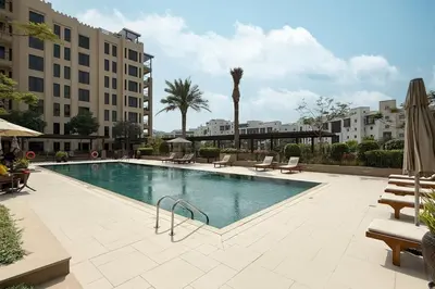 a large swimming pool with chairs and buildings at StayMada - Lamtara Near Burj AlArab Beach Access in Dubai