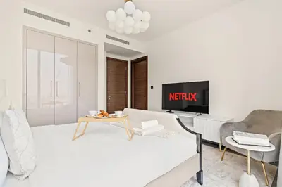 a white living room with a couch and a tv at VayK - Modern 2BR with Pool View in Sobha Hartland in Dubai