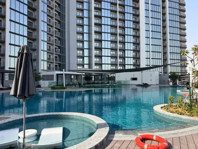 a swimming pool with an umbrella and chairs and a building at Luxury 2BR in Sobha Hartland in Dubai