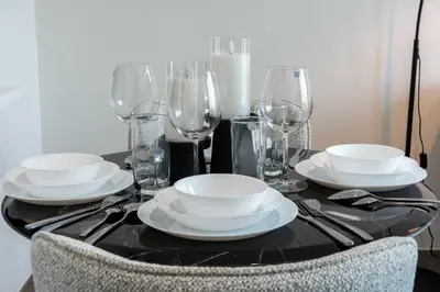 a black table with white plates and glasses on it at TRPS - Alef Noon, JVC - Brand New - Luxury Furnished 1BR - Prime JVC Location in Dubai