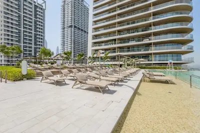 a row of chaise lounges and chairs next to a building at Partial Sea Views with Private Beach Access, Near Dubai Marina and Palm Jumeirah, Grand Bleu Tower by Elie Saab, Tower 2, Emaar Beachfront by Deluxe Holiday Homes in Dubai
