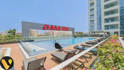 a swimming pool with lounge chairs and a building at Vogue Al Furjan Pearlz by Danube near Ibn Battuta Mall, One Bedroom Apartment with Terrace and vibrant community view, Access to all Amenities, Walkable to Al Furjan Metro Station in Dubai