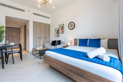 a bedroom with a large bed and a desk at Cozy Studio with Peaceful Community Views, Just Steps from Parks and Circle Mall, Oxford 212, JVC by Deluxe Holiday Homes in Dubai