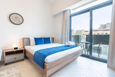 a bedroom with a bed and a balcony with a clock at Cozy Studio with Peaceful Community Views, Just Steps from Parks and Circle Mall, Oxford 212, JVC by Deluxe Holiday Homes in Dubai
