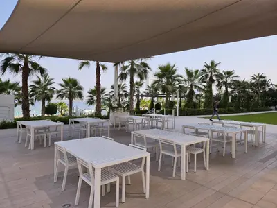 a group of tables and chairs on a patio with palm trees at Beach Please in Dubai