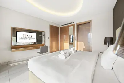 a white bedroom with a bed and a flat screen tv at BLVD - Damac Paramount with Burj Khalifa View in Dubai