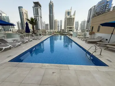 a large swimming pool with chairs and a city skyline at Daniels 2BR with Maid Room at Liv Residency with Marina View in Dubai