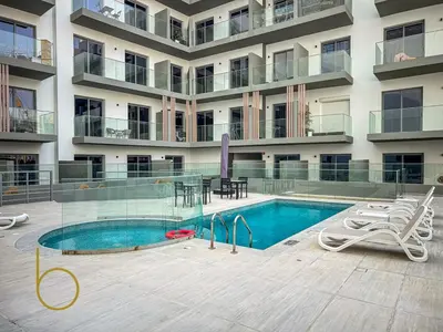 an apartment building with a swimming pool in front of a building at Bookable - Studio Room, Bali Residences JVT in Dubai