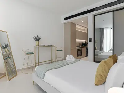 a white bedroom with a large bed and a kitchen at Welhome - Modern Gold Accents Studio in JVC with Balcony in Dubai