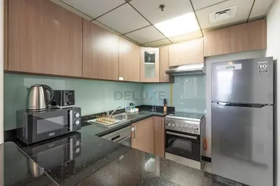 a kitchen with wooden cabinets and a stainless steel refrigerator at Walking Distance to Circle Mall and Community Parks, 18 Minute Drive to Dubai Marina and JBR Beach, Crystal Residence, JVC by Deluxe Holiday Homes in Dubai