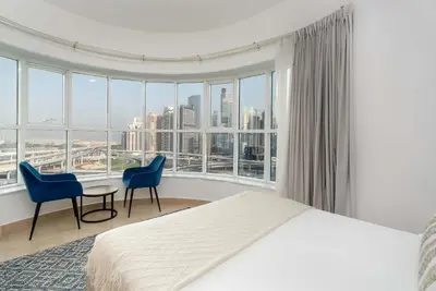 a bedroom with a bed and chairs and a large window at Modern 1BR with City View - Balcony - Near Metro in Dubai