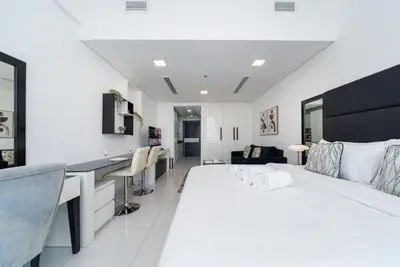 a white bedroom with a large bed and a desk at Sleek and Spacious Sports City Studio in Dubai