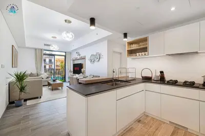 a kitchen with white cabinets and a living room at Cozy 2-BR at Belgravia Square in Dubai