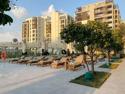a row of lounge chairs with umbrellas and trees at FIRST CLASS 2BR Creek Beach Comfort & Style in Dubai