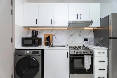 a kitchen with white cabinets and a washer and dryer at Gala Guests - Serene Lakeside Residences Production City in Dubai