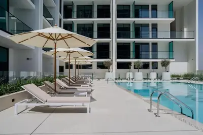 a pool with lounge chairs and umbrellas next to a building at HAVN - Bright & Cozy Studio at Binghatti Azure JVC in Dubai