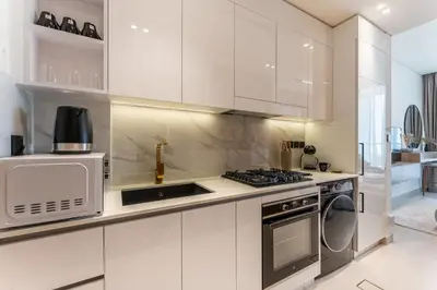 a white kitchen with a stove and a microwave at HAVN - Bright & Cozy Studio at Binghatti Azure JVC in Dubai