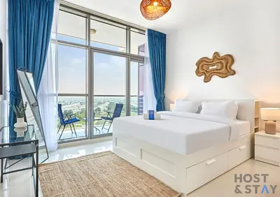 a white bedroom with a bed and a balcony at Radiant & Sunny Living - 1BR in ORchid DAMAC Hills in Dubai