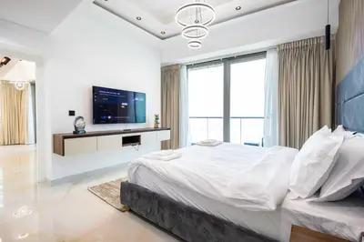 a white bedroom with a large bed and a flat screen tv at Luxuries Sky View Apartment in Dubai