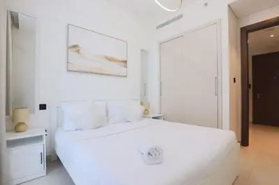 a white bedroom with a white bed and a painting on the wall at Cosy 1BR in Sobha Hartland in Dubai