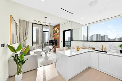 a kitchen with white cabinets and a living room with windows at Golden Stays - Private Pool in Binghatti Gardenia I Coastal Charm I Luxe 2BR Escape in Dubai