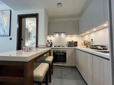 a kitchen with white cabinets and a counter with bar stools at The Crest Sobha Hartland in Dubai