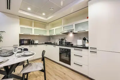a kitchen with white cabinets and a dining table at FIRST CLASS 2BR Luxe & Lively Living in Dubai