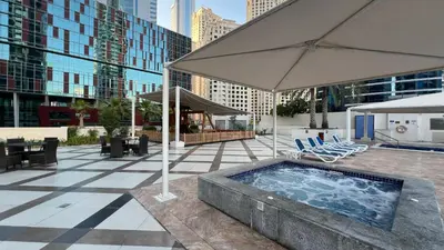 a swimming pool with an umbrella and chairs and tables at Modern 1BR Apt With Access to Jacuzzi, Sauna & Pool in Dubai