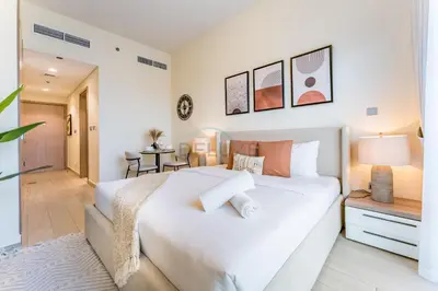 a bedroom with a white bed and a table at Close to Meydan Racecourse and Ras Al Khor Wildlife Sanctuary, And a Quick Drive to Downtown Dubai and the Iconic Burj Khalifa - Azizi Riviera 44, Meydan by Deluxe Holiday Homes in Dubai