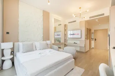 a white bedroom with a white couch and a tv at New Studio Aura JVC Pool Gym Sauna Padel court in Dubai