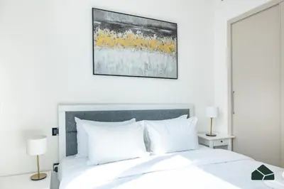 a white bed with white pillows and a painting on the wall at Cozy 1BR for 3 with Community View by BMS in Dubai