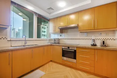 a kitchen with wooden cabinets and a large window at SkyHigh 4BR Penthouse Marina Views & Game Lounge Pool Table PS5 in Dubai