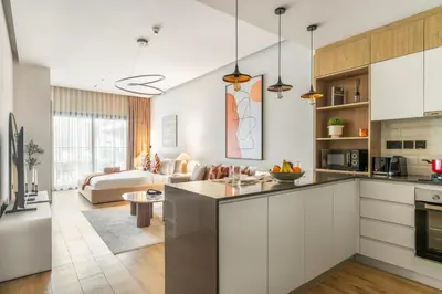 a kitchen with white cabinets and a living room at FIRST CLASS Studio Minimalist Chic Retreat in Dubai