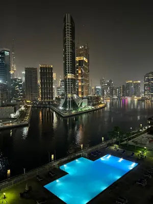a view of a city at night with a large blue pool at The Haven Burj Khalifa View - 1BR Business Bay with Balcony&Pool in Dubai