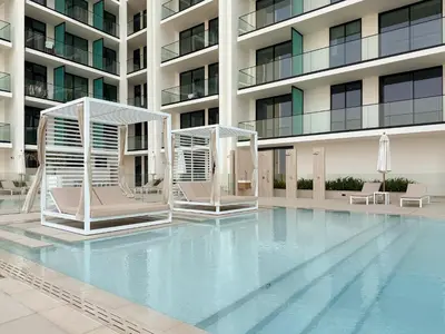 a swimming pool with two chairs and a building at Modern Studio with Pool & Gym - Prime JVC Location in Dubai