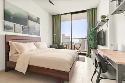 a bedroom with a large bed and a desk and a desk at Modern Studio with Pool & Gym - Prime JVC Location in Dubai
