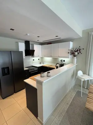 a kitchen with white cabinets and a black refrigerator at Family Villa, Sleeps up to 9 in JVT and Large garden in Dubai